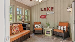 L’intérieur d’un chalet accueillant, avec un canapé, deux fauteuils, une lampe, une pancarte indiquant « LAC », et une petite table sur laquelle est posée une plante.