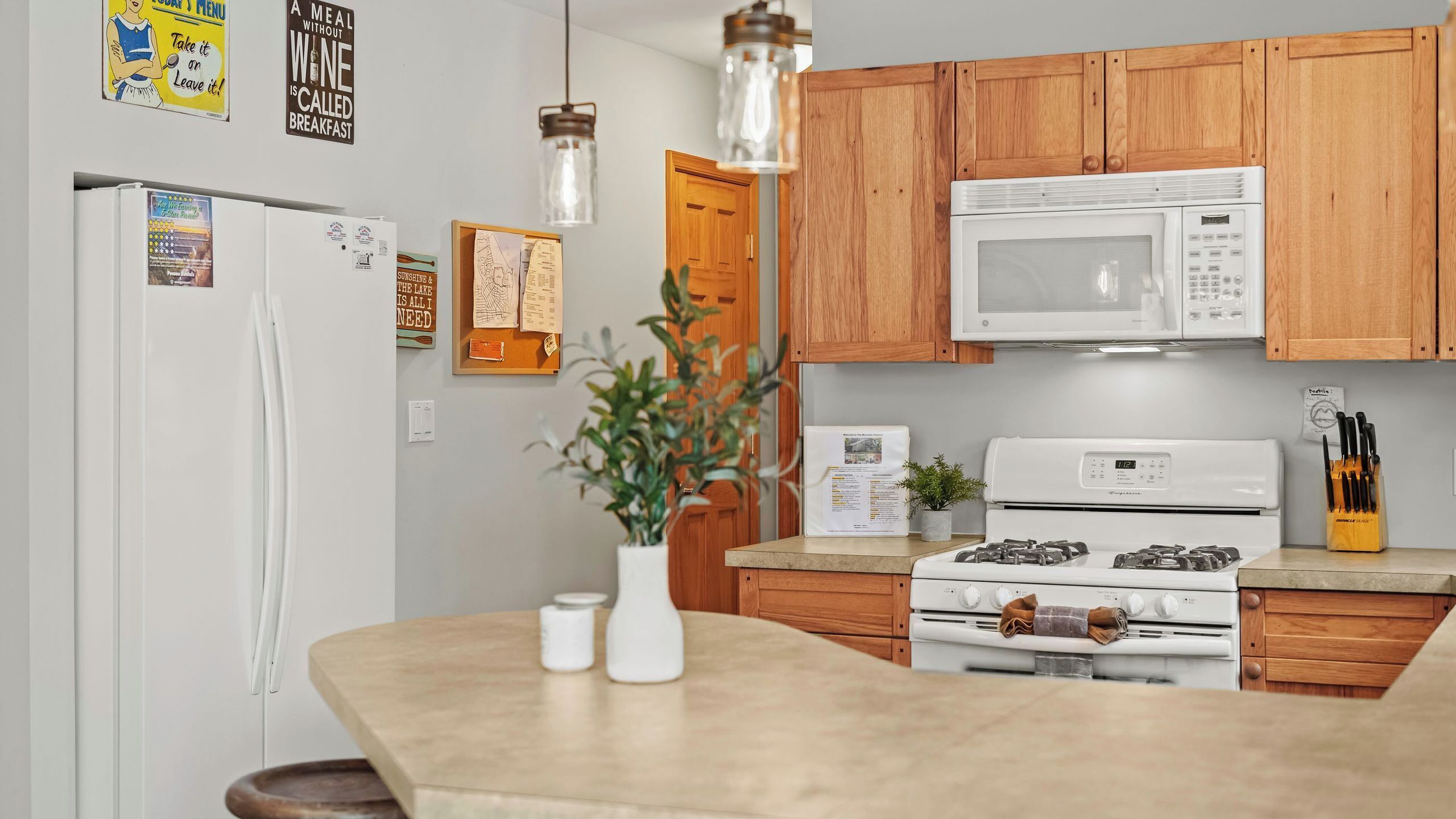 A kitchen with wooden cabinets, a white refrigerator, a microwave, a stove, and hanging pendant lights.
