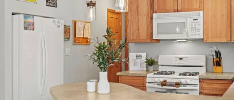 A kitchen with wooden cabinets, a white refrigerator, a microwave, a stove, and hanging pendant lights.