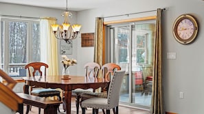 A dining room with a wooden table, chairs, a chandelier, and a large window with curtains.