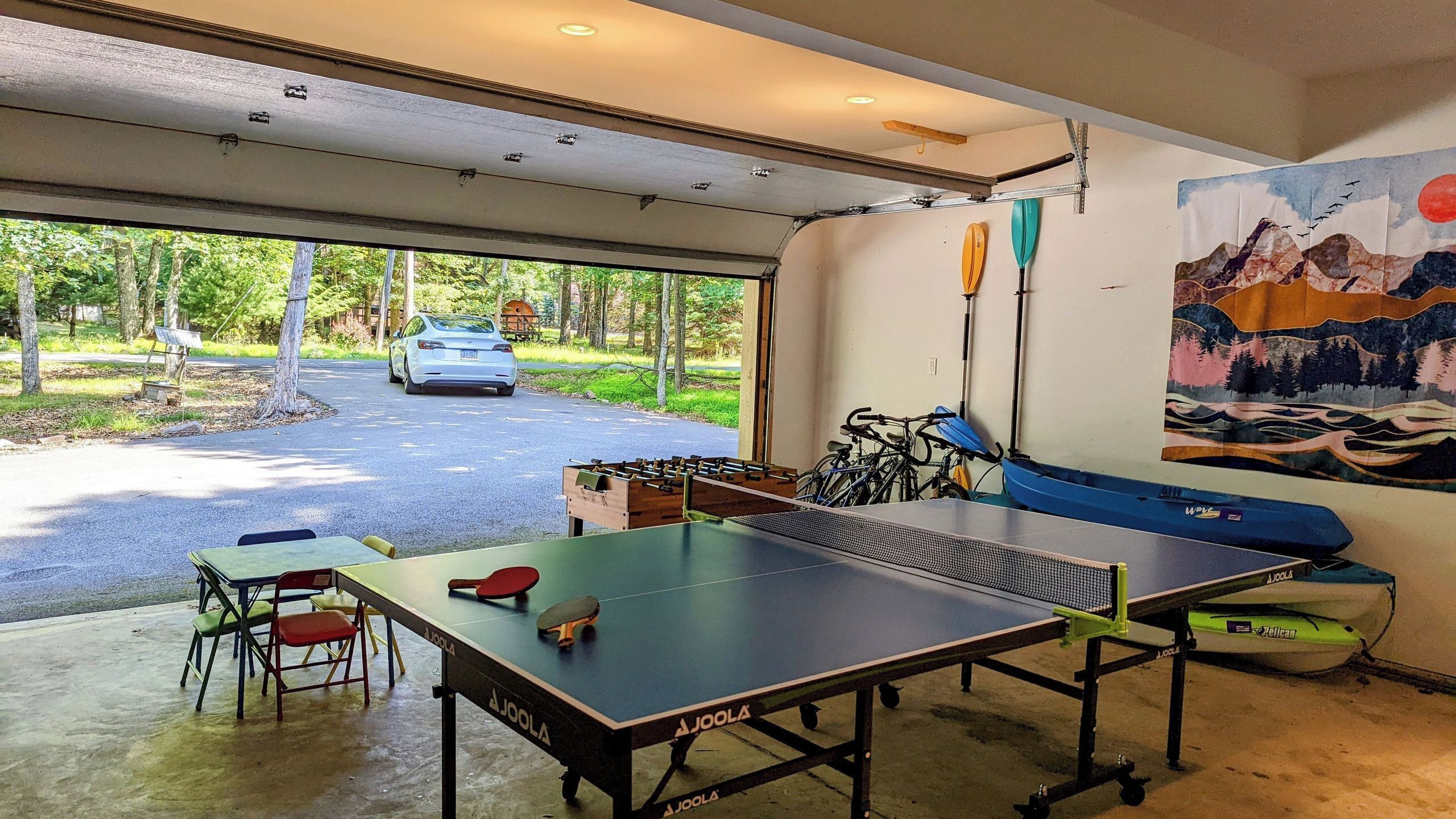A ping pong table, bicycles, and a painting in a garage.
