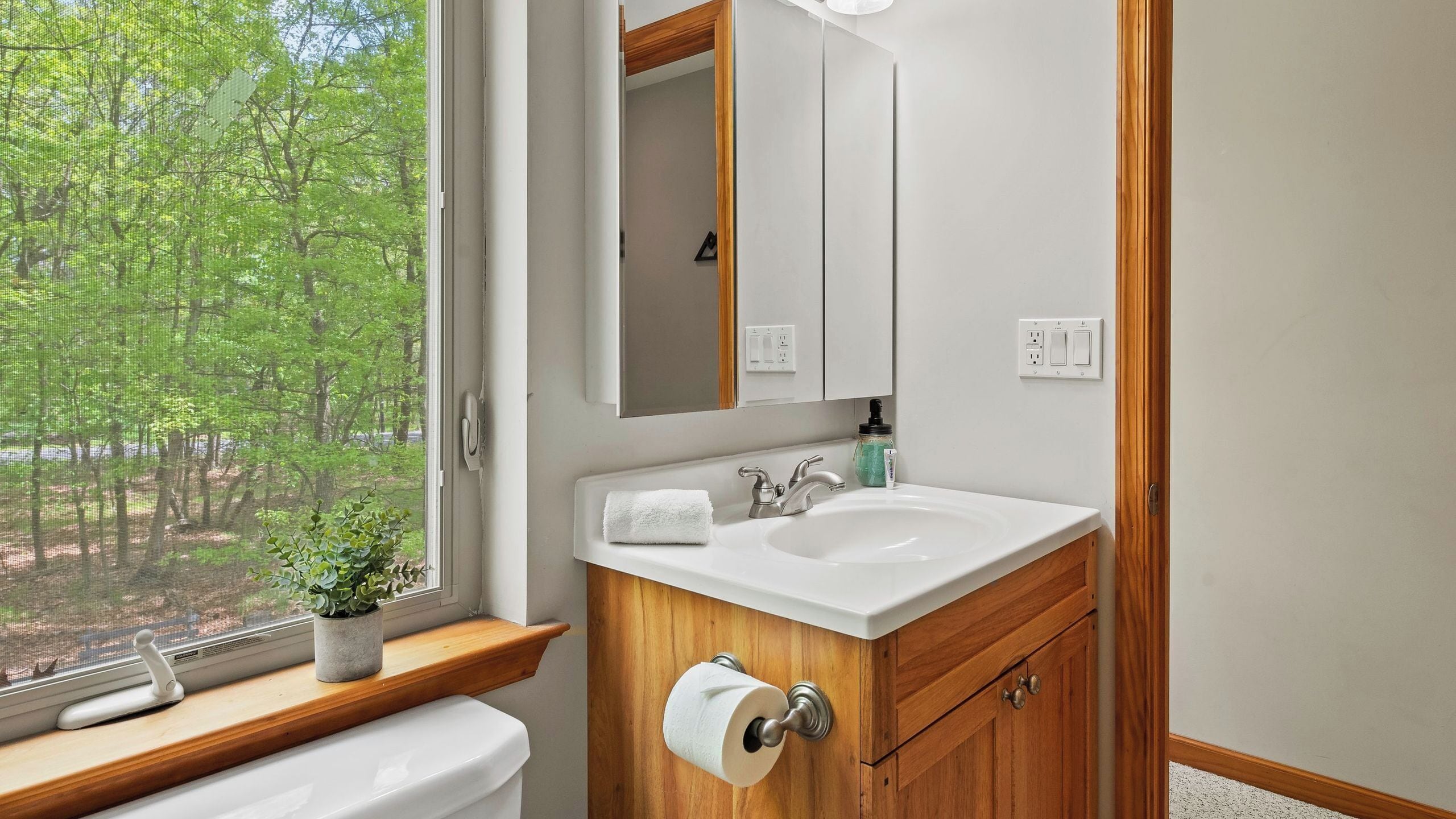 A bathroom with a window, a sink, a mirror, and a toilet.