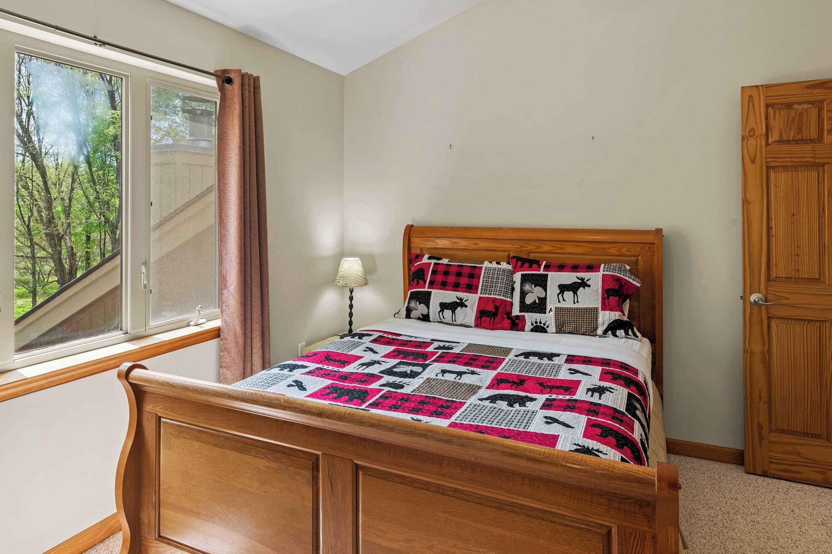 A bedroom with a wooden bed, a window with curtains, and a view of trees.