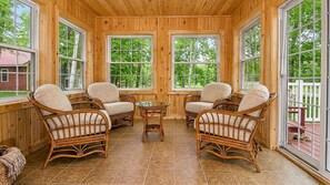A wooden-paneled room with wicker furniture, large windows, and a view of greenery outside.