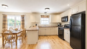 Una cocina con armarios de madera, un refrigerador negro, una estufa y un comedor con mesa y sillas.