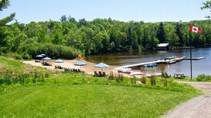 A lakeside campsite with picnic tables, umbrellas, and a dock with boats.
