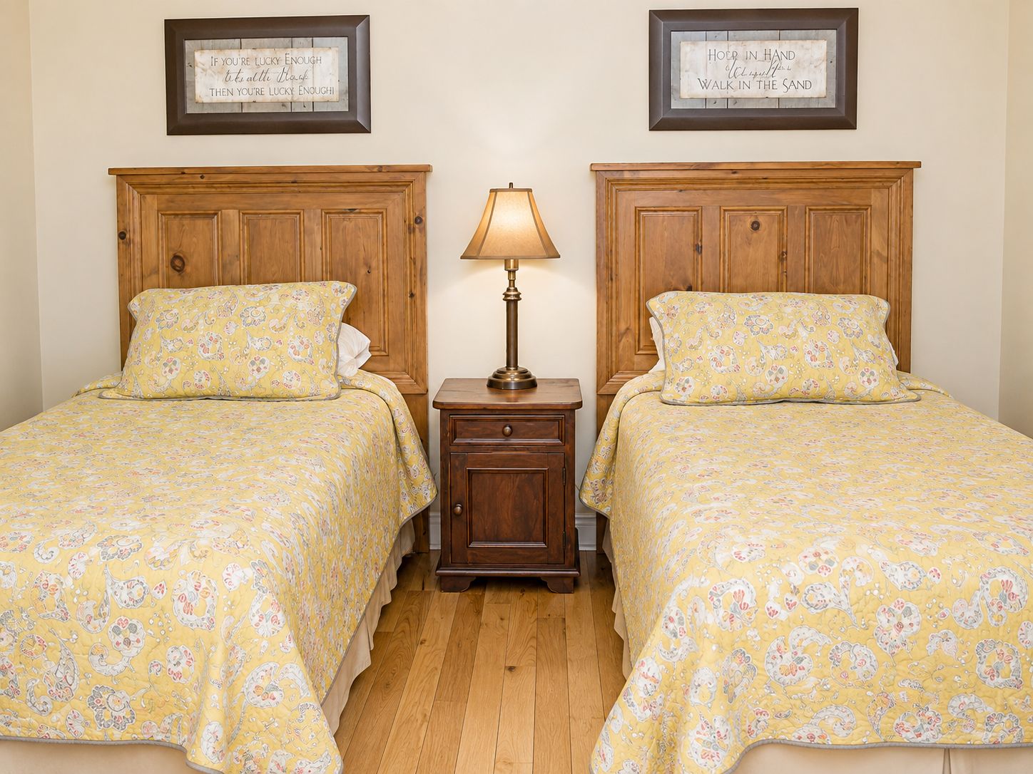 Ein Doppelzimmer mit zwei Betten, jeweils mit Holz Kopfteil und passender Blumenbettwäsche. Dazwischen befindet sich ein Nachttisch mit einer Lampe.