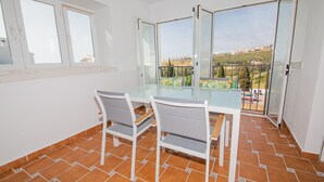 Varanda com mesa e cadeiras de vidro, piso de azulejos e vista para uma área residencial.