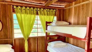 A wooden cabin room with bunk beds, a window with green curtains, and a wooden ceiling.