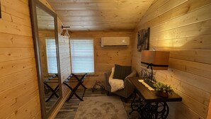 L’intérieur chaleureux d’un chalet avec des murs en bois, un coin repas comprenant une table et des chaises, un petit canapé, un miroir et un vélo.