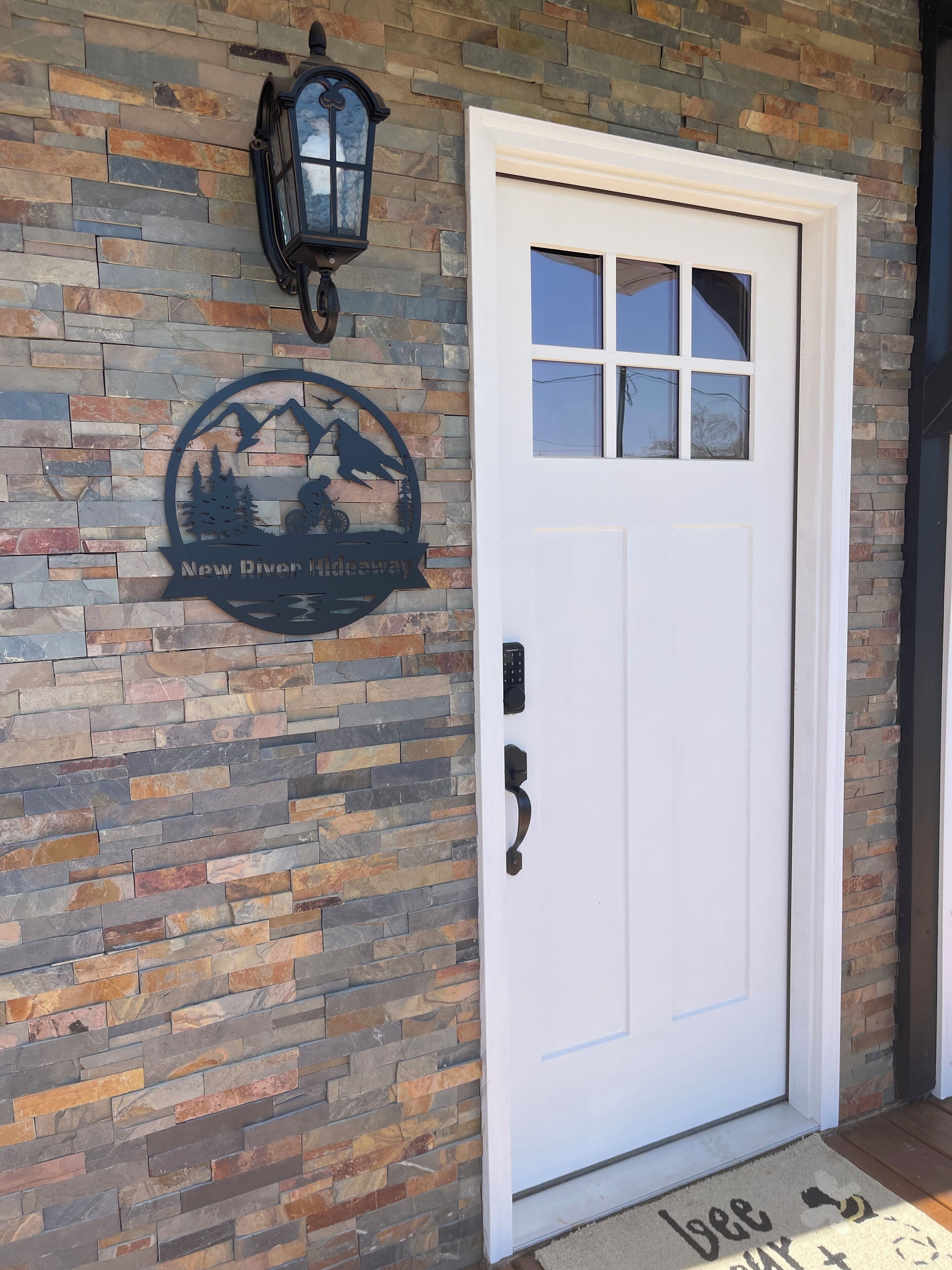Puerta blanca con un panel de vidrio, cerradura electrónica y felpudo con la palabra 'Bee' y el dibujo de una abeja.