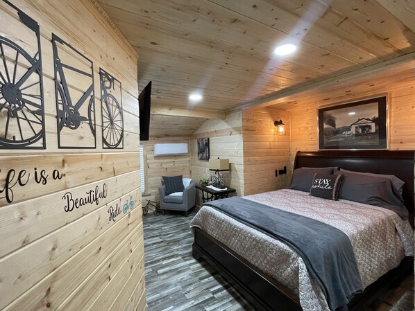 A cozy wooden cabin bedroom with a bed, a chair, and a wall with bicycle cutouts. - New River Hideaway - Walking Distance to Historic Downtown Galax Virginia (Galax)