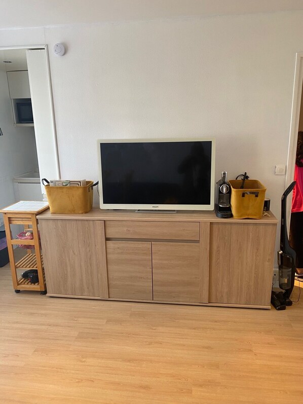 Un mueble de madera con un televisor de pantalla plana, dos contenedores de almacenamiento amarillos y una mesita con un estante.