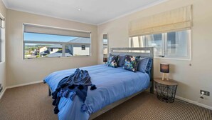 A bedroom with a large bed, a window with a view, a bedside table with a lamp, and a power outlet. - Fresh on Fletcher - Taupo Holiday Home (Taupo)