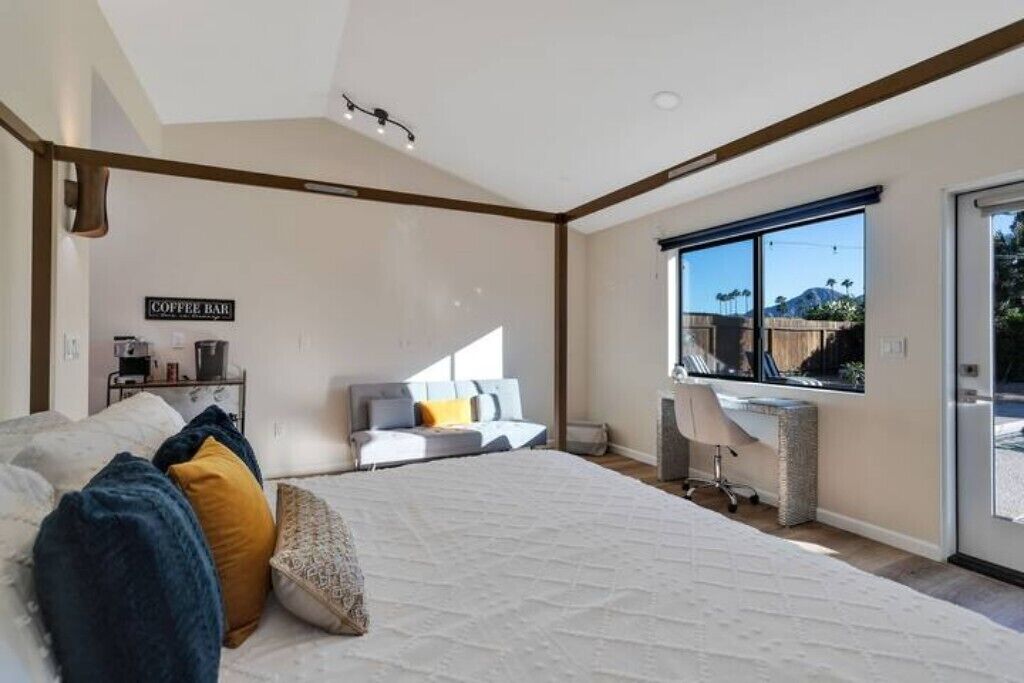 Ein modernes Schlafzimmer mit großem Bett, einer Kaffeestation und einem Schreibtisch neben einem großen Fenster.