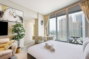 Habitación de hotel con una cama grande, una mesita pequeña, una silla, una planta en maceta y vistas de edificios altos.