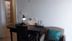 A small, furnished room with a dining table, two chairs, a sofa with a teal pillow, and a lamp.