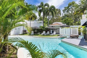 A swimming pool with lounge chairs and umbrellas, surrounded by palm trees and a white building. - Swaying Palms and Salt Air—A Dreamy Tropical Haven (Palm Cove)