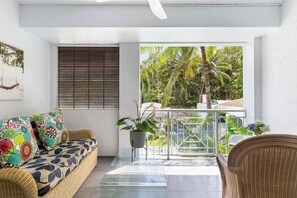 Un soggiorno moderno con un divano, una poltrona, un balcone con vista su palme e un’amaca sospesa.