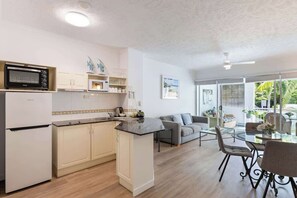 Una cucina moderna con mobili bianchi, un forno a microonde e un'isola piccola. C'è una zona pranzo con un tavolo in vetro e sedie, e un divano.
