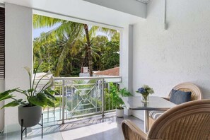 Un balcone con vista su palme, un tavolino in vetro, mobili in vimini e piante in vaso.