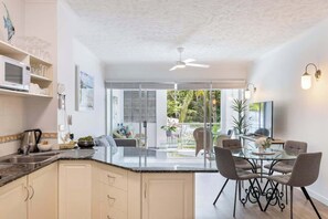 A modern kitchen with a central island, a dining area with a glass table, and a view of the outdoors.