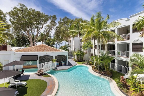 A resort with a swimming pool, outdoor seating, and lush tropical landscaping.