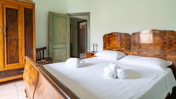 A neatly made bed with white linens and rolled towels, a wooden wardrobe, and a wooden headboard.