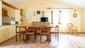A dining area with a wooden table and chairs, a television, and a kitchen in the background.