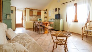 A cozy living room with a sofa, a dining table with chairs, and a kitchen area with wooden cabinets and a microwave.