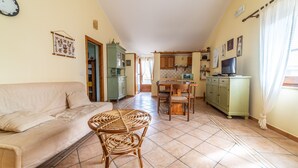 A cozy living room with a sofa, a wicker table, and a kitchen area with cabinets and a TV.