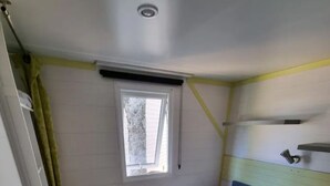 Ein kleiner, schmaler Raum mit einem Bett, einem Fenster und einem Deckenventilator.