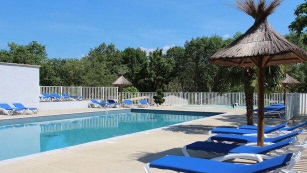 Ein Swimmingpool mit blauen Liegestühlen und einem Reetdachschirm.