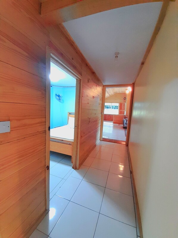Un pasillo con paredes de madera y suelo de baldosas que conduce a un dormitorio con cama y ventana.