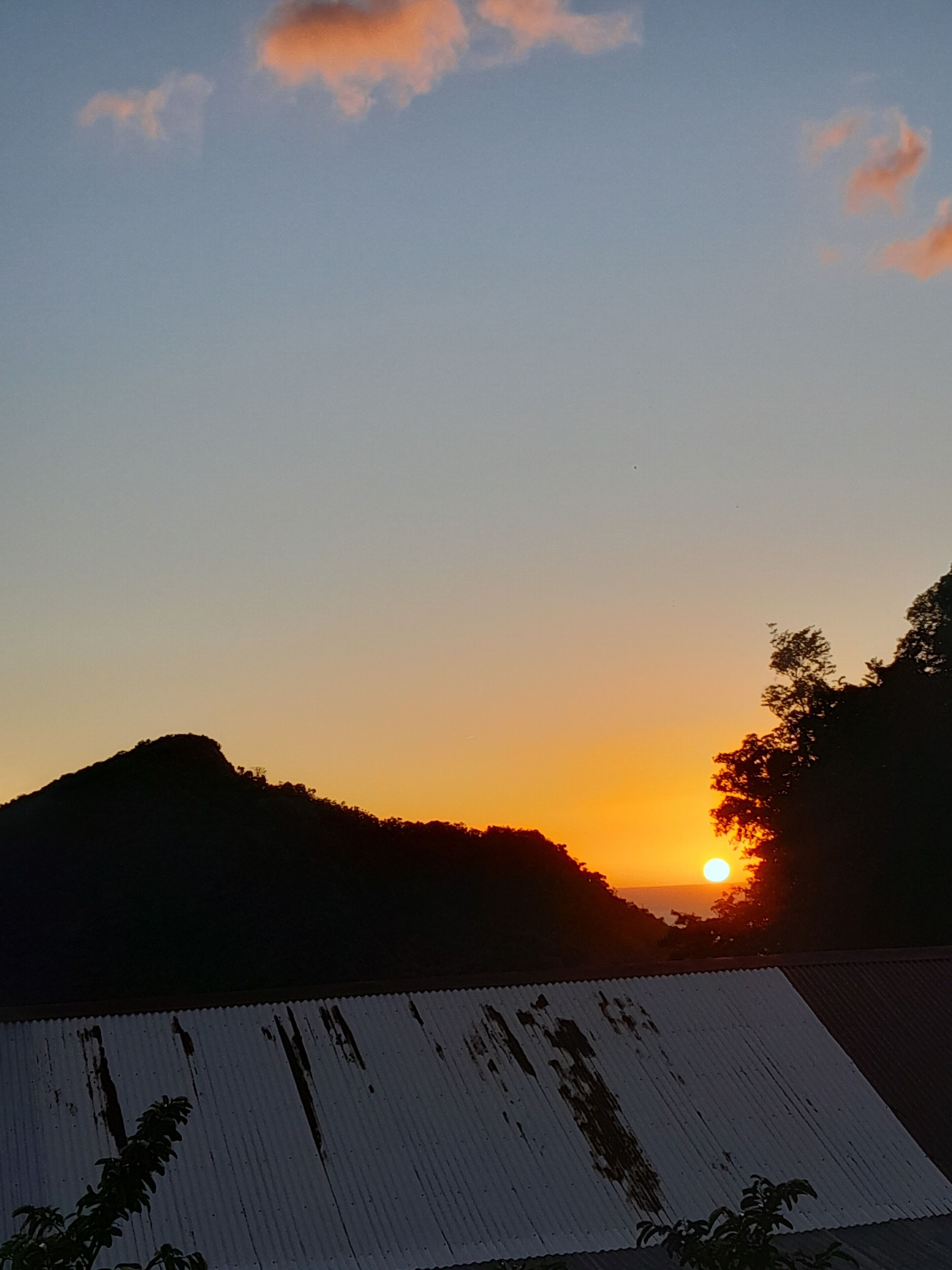 A sunset over a hilly landscape with a corrugated metal roof in the foreground.