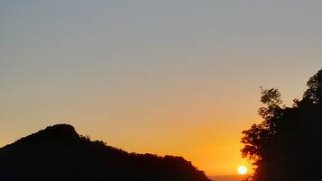 A sunset over a hilly landscape with a corrugated metal roof in the foreground.