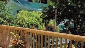 A person lying on a sun lounger on a wooden deck with a view of a house and greenery in the background. - Pinard's Mountain Resort - Cottage 10 (Pointe Michel)