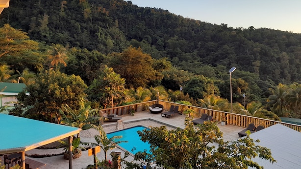 A pool area with lounge chairs, a wooden deck, and a view of a forested hillside. - Pinard's Mountain Resort - Cottage 10 (Pointe Michel)