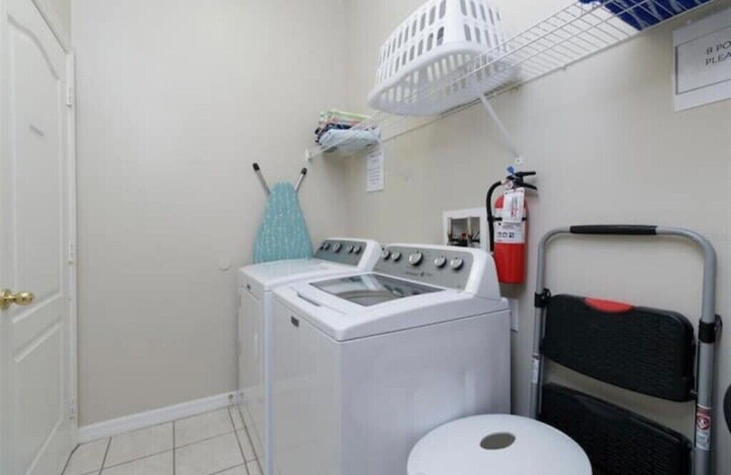 A laundry room with a washing machine, a dryer, a fire extinguisher, and a folding chair.
