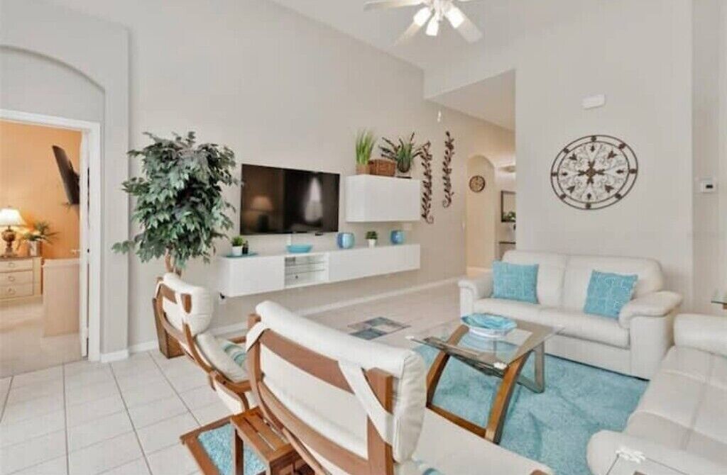 A modern living room with a flat-screen TV, white sofas, a coffee table, and a large plant.