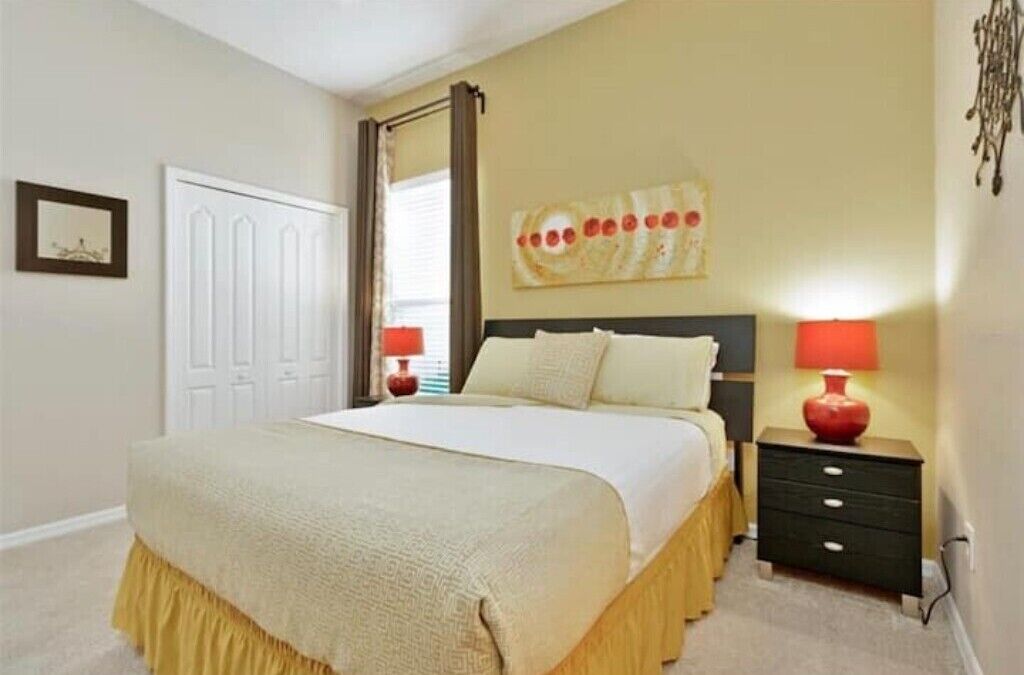 Une chambre à coucher avec un lit, des tables de chevet, une porte et un mur orné d’un tableau.