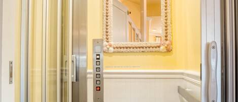 A narrow elevator with a mirror and control panel, white walls, and a wooden floor.