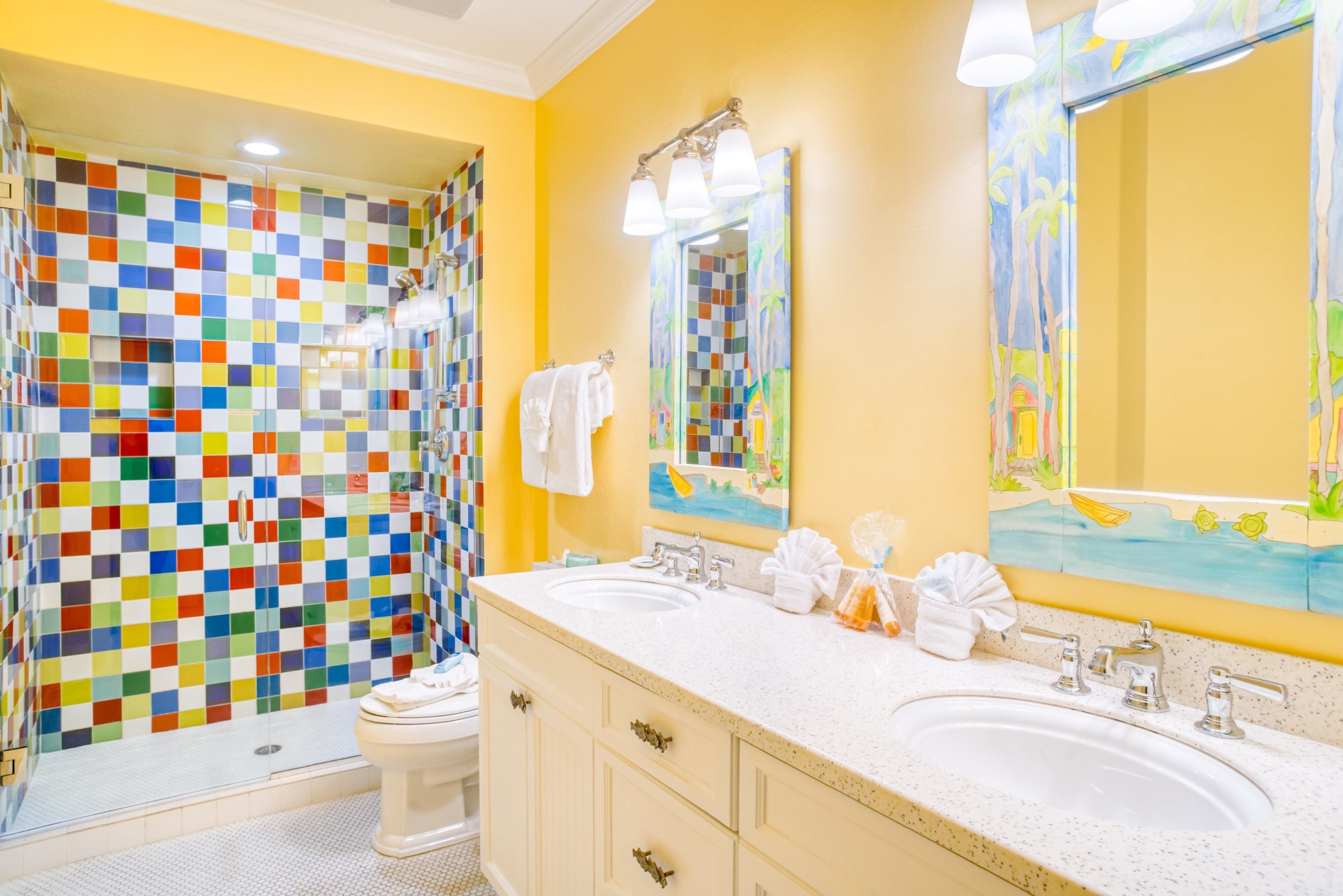 A bathroom with a colorful mosaic wall, a large mirror, and a double sink vanity.