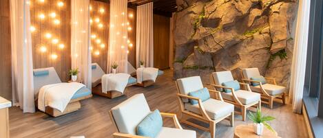 A spa room with massage chairs, a wooden floor, and a rock wall.