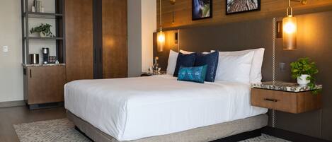 A modern bedroom with a large bed, wooden headboard, bedside tables, and a built-in shelf with plants.