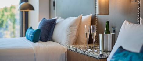 A hotel room with a bed, bedside table, and a bottle of champagne.