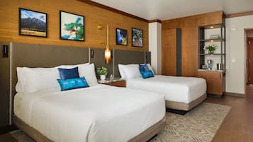 Two single beds with white linens and blue decorative pillows, a wooden headboard, a wall-mounted shelf with books, and a framed picture of a mountain landscape.