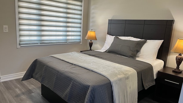 Un dormitorio con una cama, dos mesitas de noche, una ventana con persianas y una lámpara sobre cada mesita.