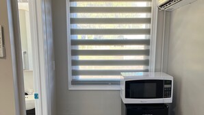 Una cocina compacta con microondas integrado, un refrigerador pequeño y una ventana con persianas.