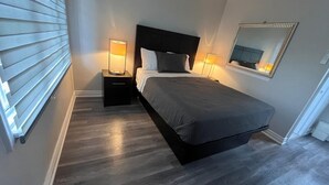 Un dormitorio con cama, dos mesitas de noche, un tocador, un espejo y una ventana con persianas.